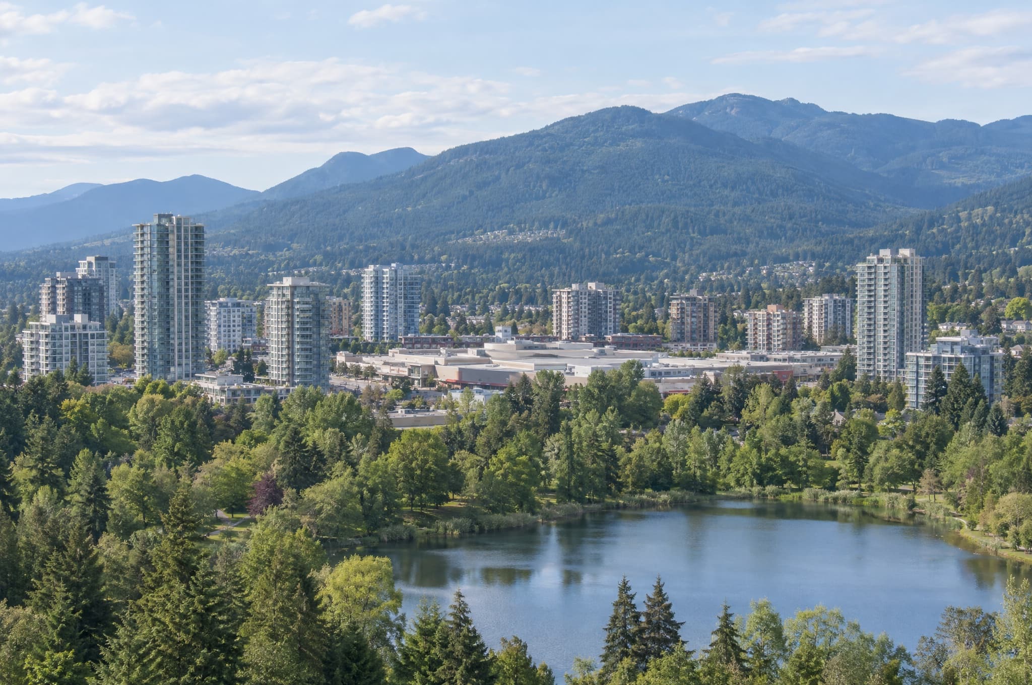 High-rise town centre above a green park and lake with snow-capped mountains behind