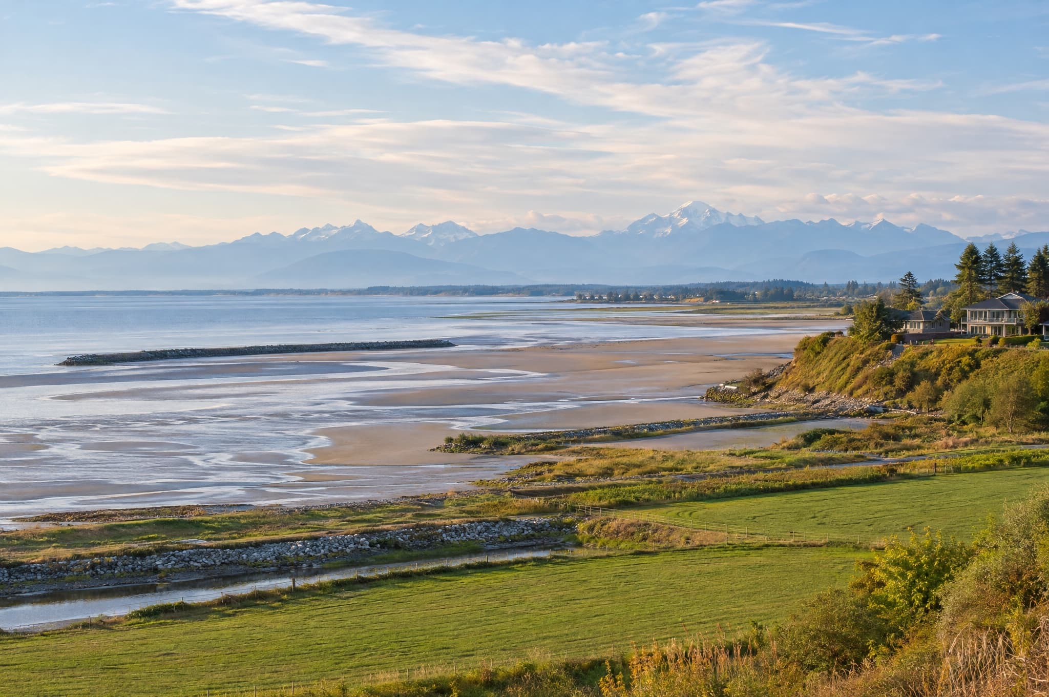 Sunset over coastal farmland, dykes and a wide sandy bay with distant mountains